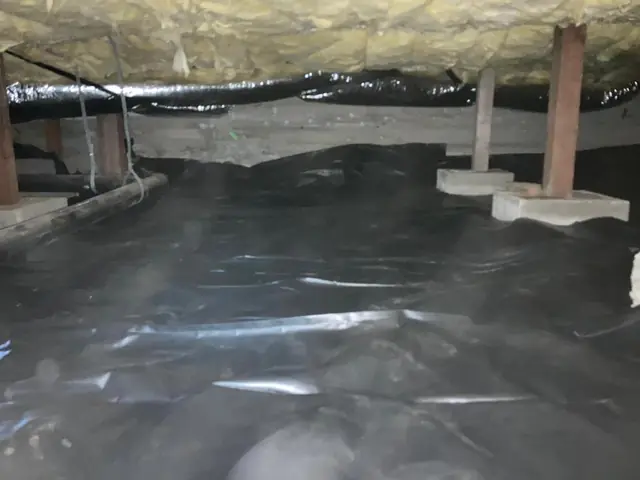 Black vapor barrier laid across a crawl space