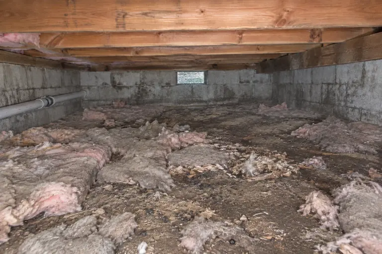 Block-wall crawl space cleanout, before: Torn insulation and debris scattered across the crawl space.