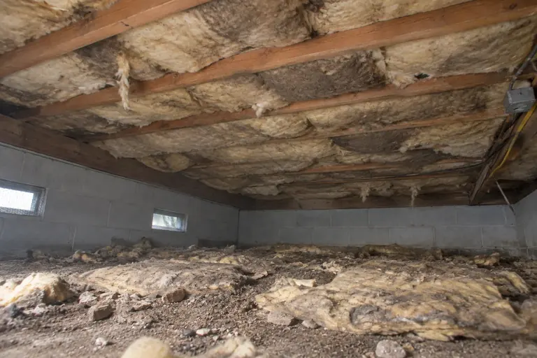 Underfloor insulation replacement, before: Sagging, worn insulation under a raised floor.
