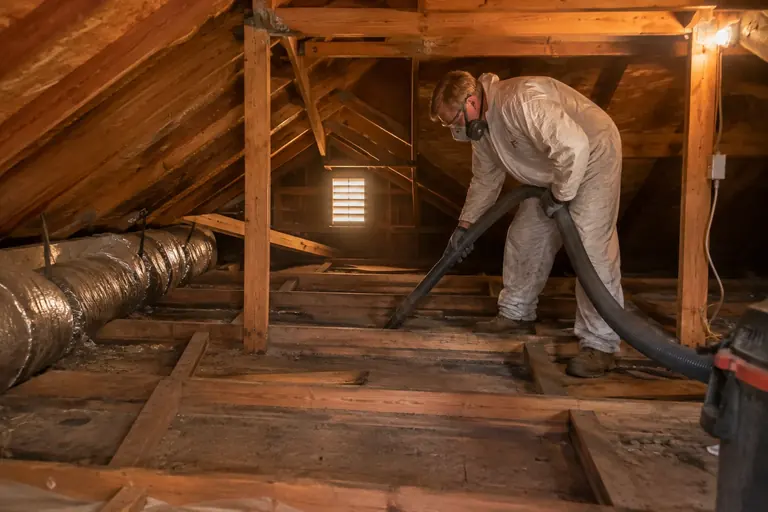 Vacuuming debris from an attic in a full protective suit.